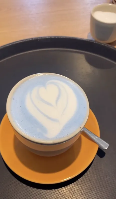 Blauer Latte mit Herz aus Milchschaum auf oranger Untertasse
